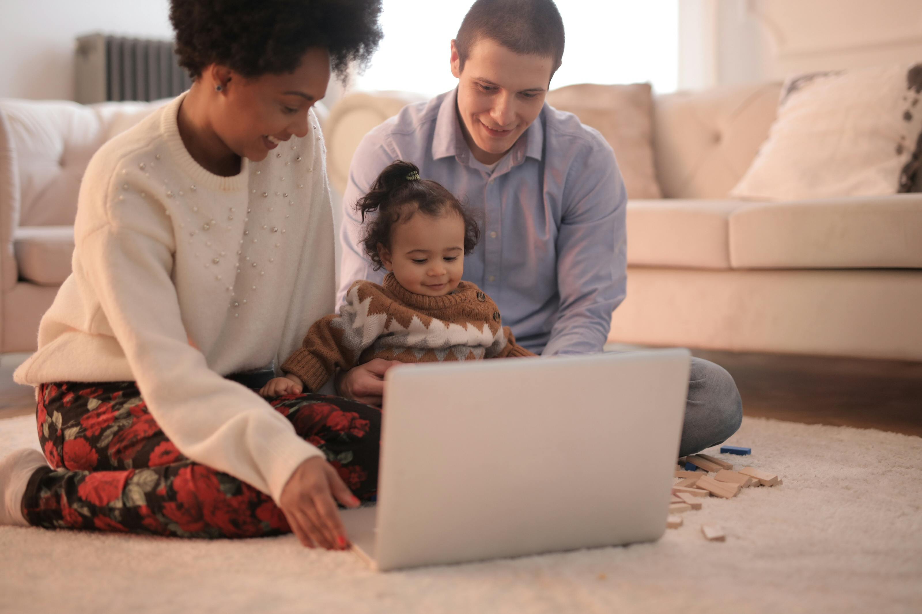 photo of family sitting on floor while using laptop