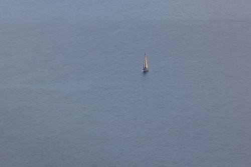 Free A solitary sailboat navigates the expansive blue ocean under a clear sky, captured in a minimalist style. Stock Photo