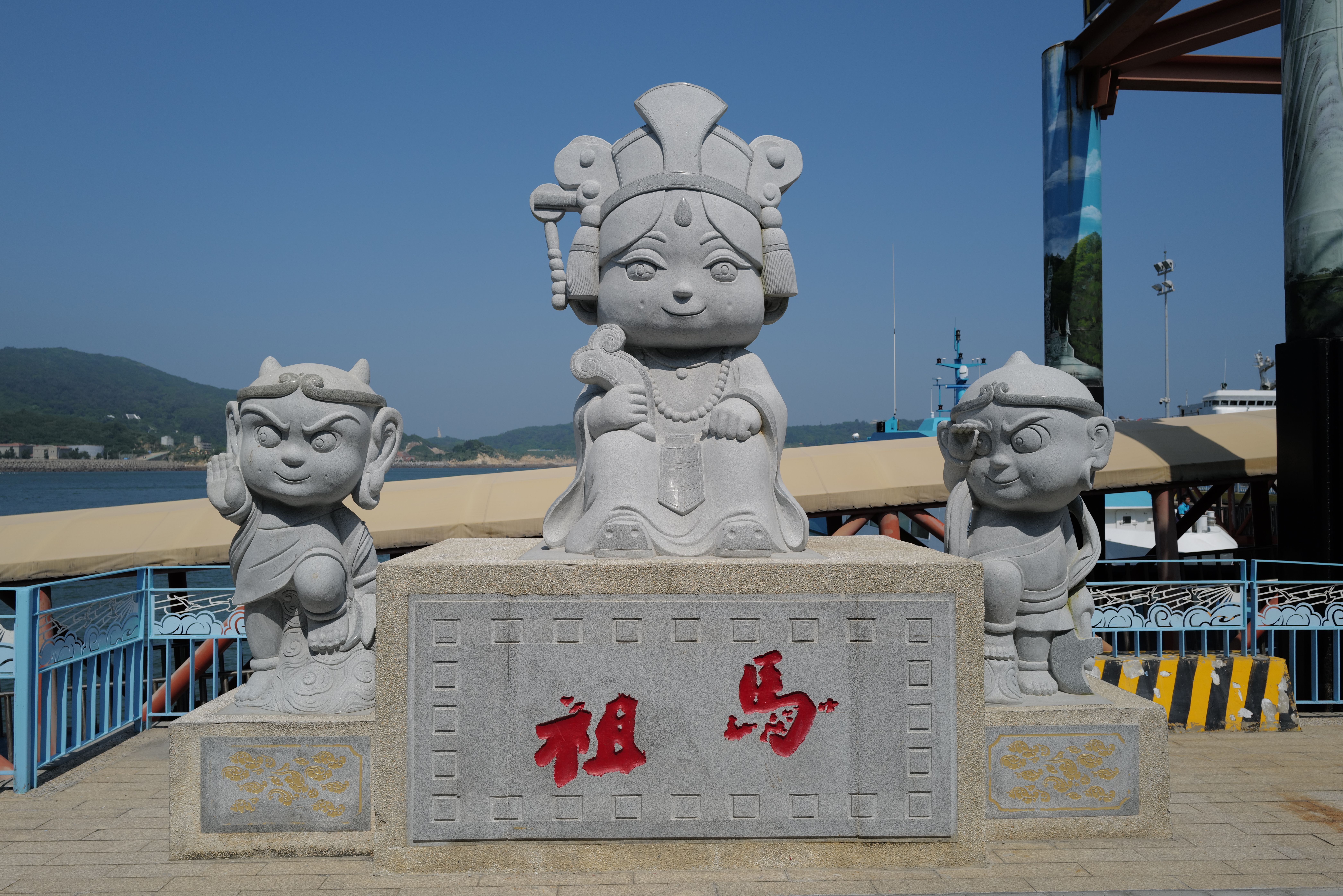 Playful stone statues with traditional attire by the seaside under a clear blue sky.
