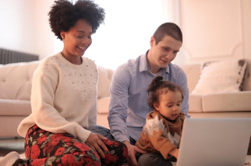 Foto Der Familie, Die Auf Boden Sitzt, Während Laptop Verwendet Wird