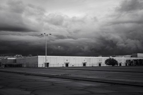 Free Black and white photo of an industrial building under stormy clouds, showcasing dramatic and moody tones. Stock Photo