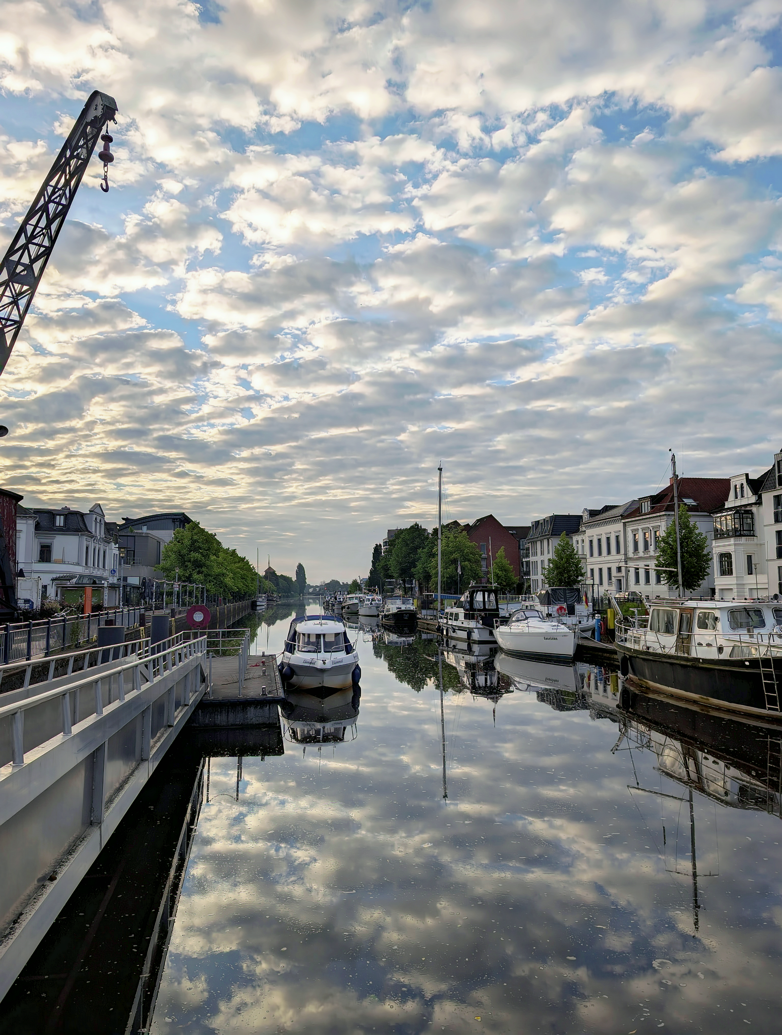 A serene canal scene with boats reflecting in calm waters under a cloudy sky.