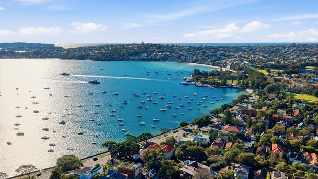 Aerial view of numerous boats on a vibrant bay in a sunny coastal city.