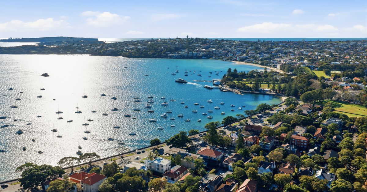 A stunning aerial shot of Sydney Harbor with sailboats and lush greenery under a clear sky.