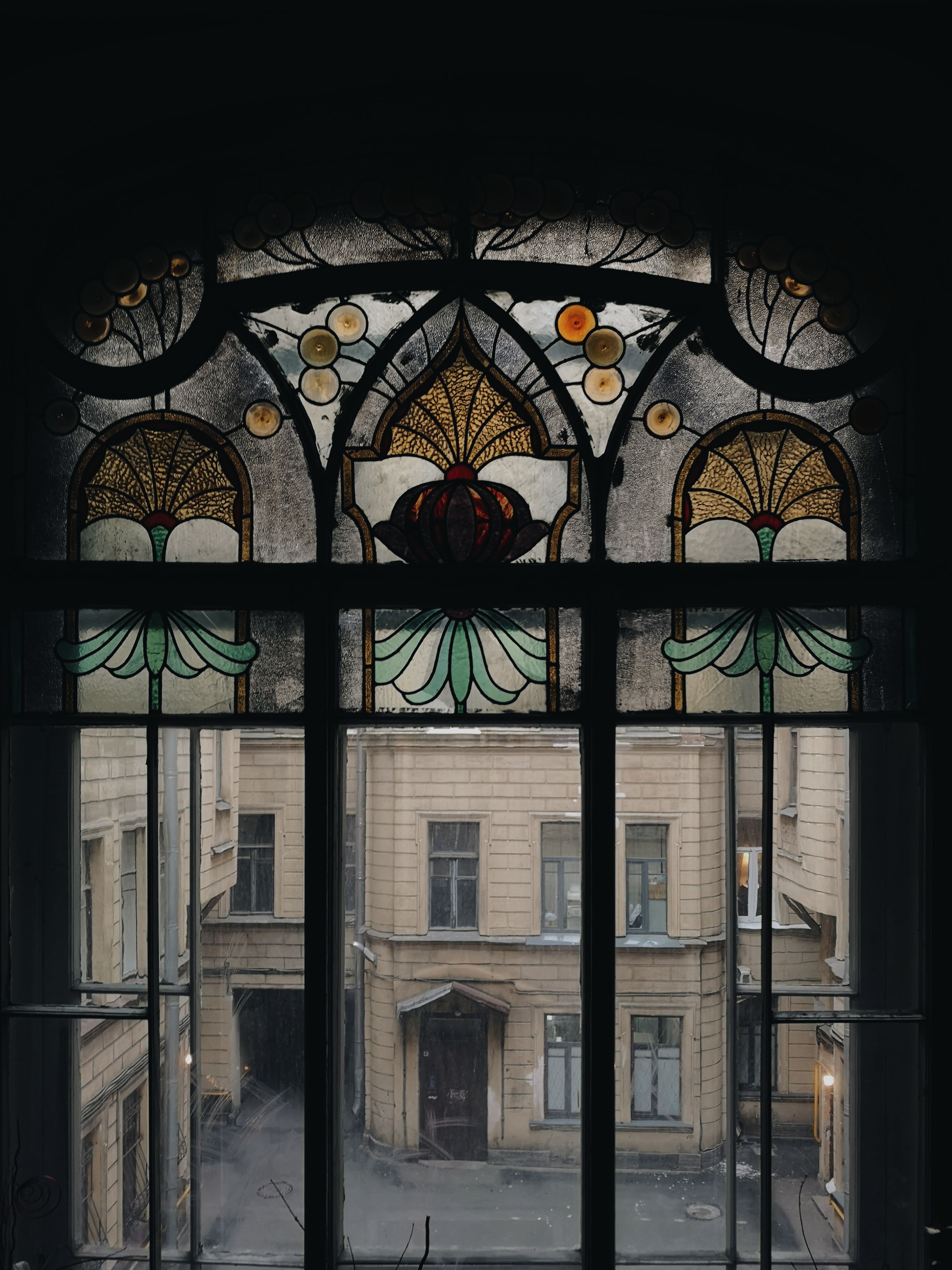 View from inside window with metal fence and mosaic decoration of stone aged residential multistage house and door near asphalt pavement