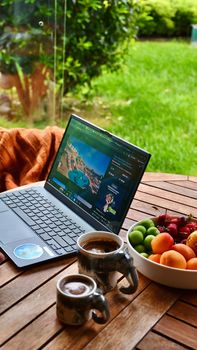 Cozy outdoor workspace with a laptop, coffee, and fresh fruits on a wooden table.