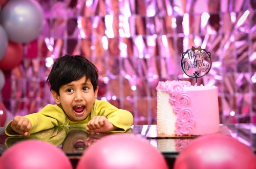 Free A South Asian child excitedly celebrates their birthday with a pink cake indoors. Stock Photo