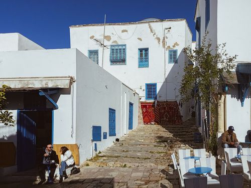 Free Sunny street scene in Sidi Bou Said, Tunisia, showcasing traditional architecture and local life. Stock Photo