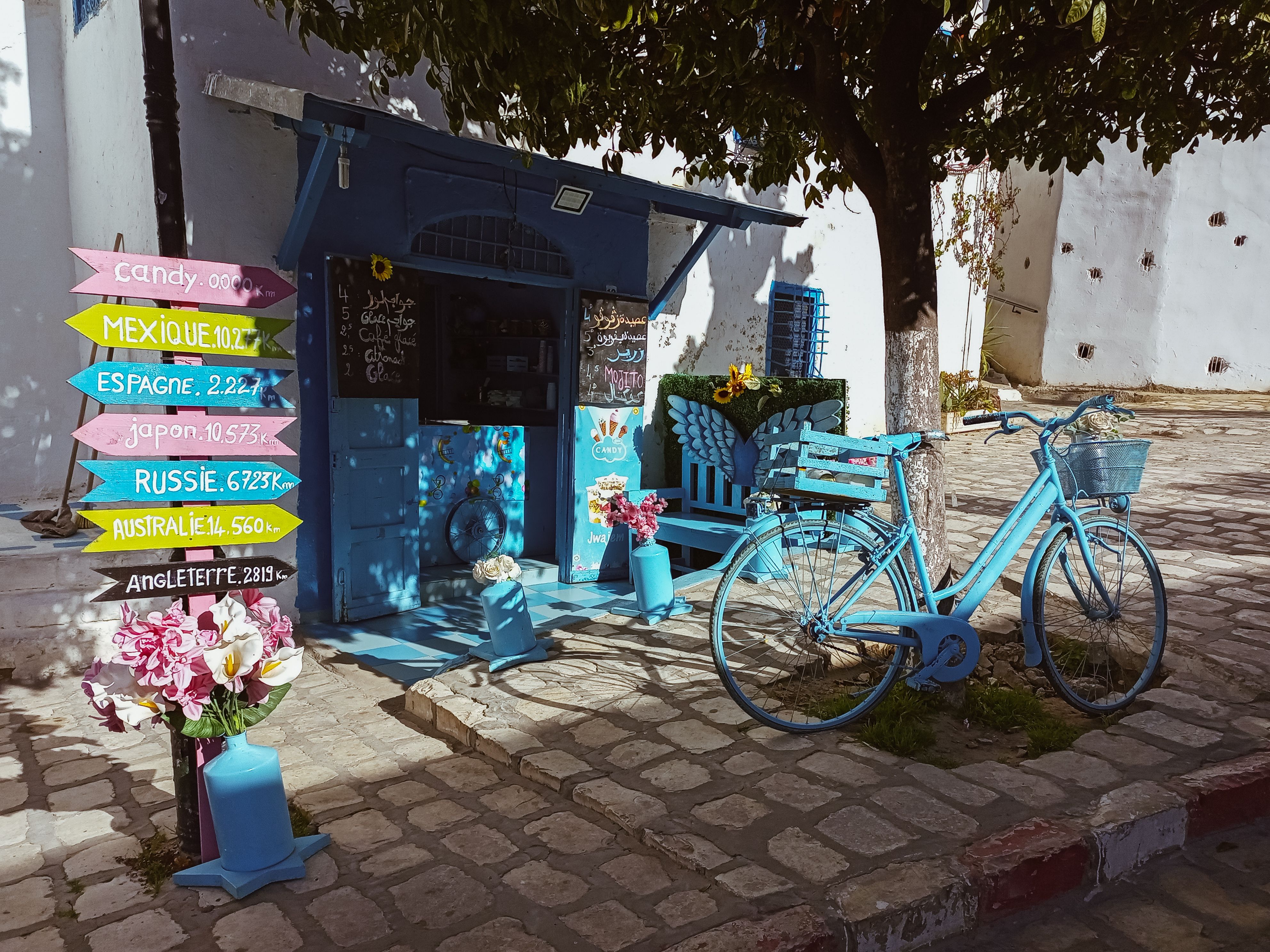A colorful street scene from Tunisia featuring a blue bicycle, vibrant signage, and a cozy shop.