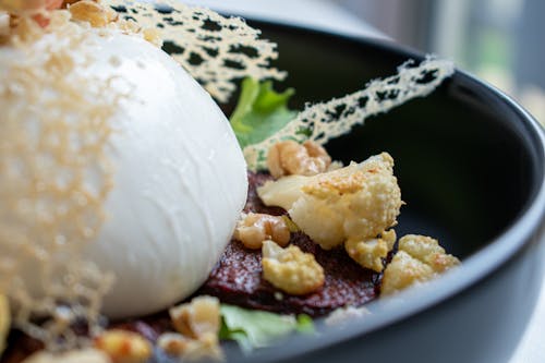 Closeup of tasty salad with golden cauliflower pieces on toasted meat slices and lettuce leaves with big ball of fresh mozzarella cheese decorated with edible grid in bowl