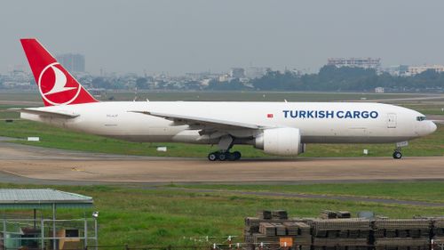 Free Turkish Cargo Boeing 777 aircraft preparing for takeoff at an airport runway with cityscape in the background. Stock Photo