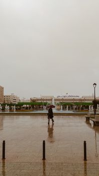 Person with umbrella on a rainy day in front of Tunis Train Station.