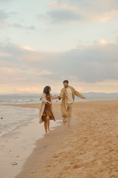 A couple enjoys a romantic walk along a sandy beach during sunset, creating a serene seaside atmosphere.