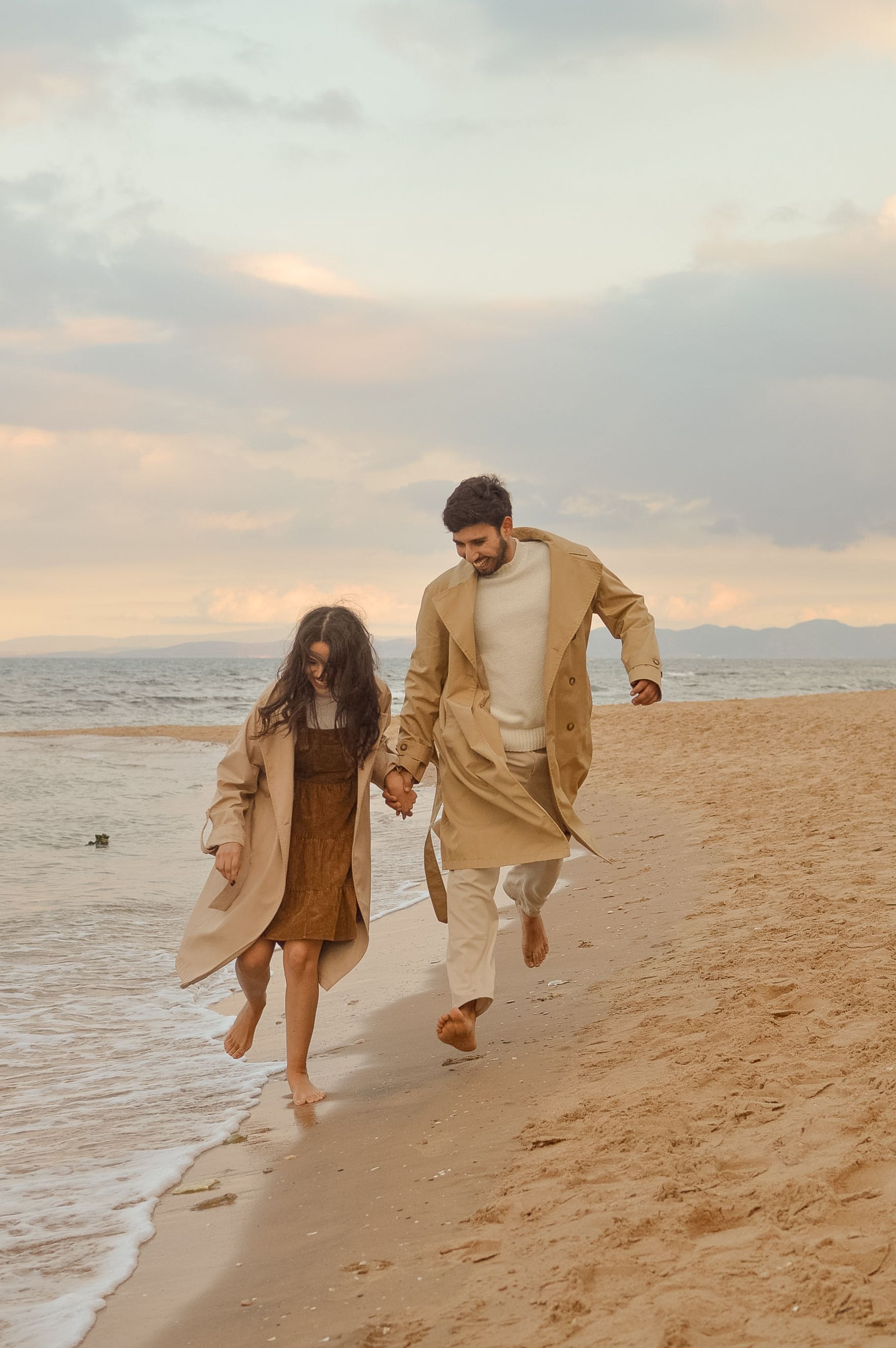 A couple walks hand in hand along the sandy beach during a romantic sunset.