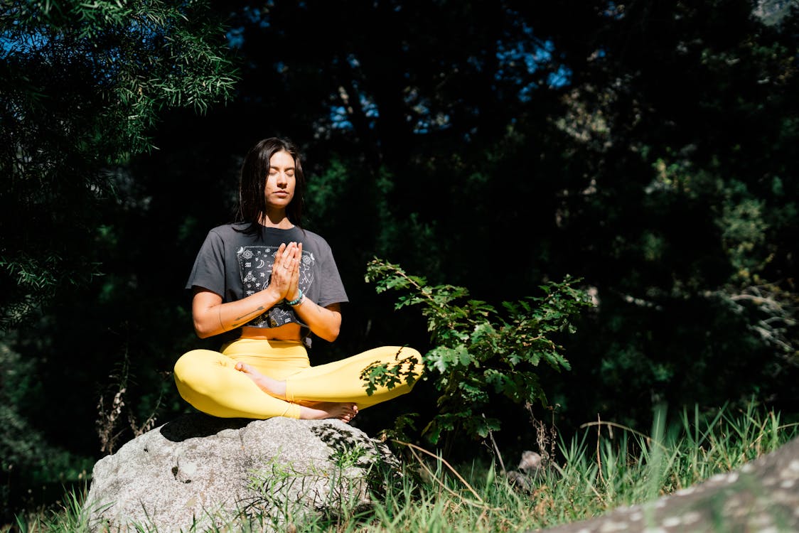 woman doing yoga while sitting on rock 