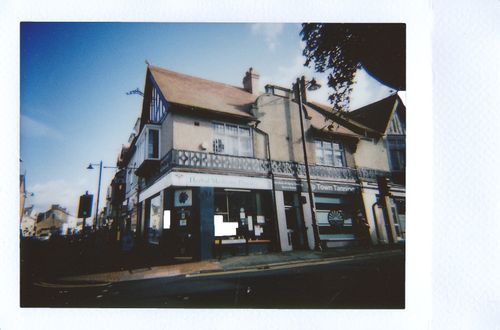 Free Instant photograph of a quaint urban building on a sunny street corner, ideal for urban and architectural themes. Stock Photo