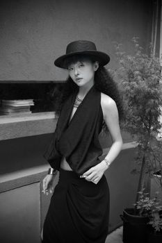 Stylish woman in black hat and attire posing elegantly outdoors.