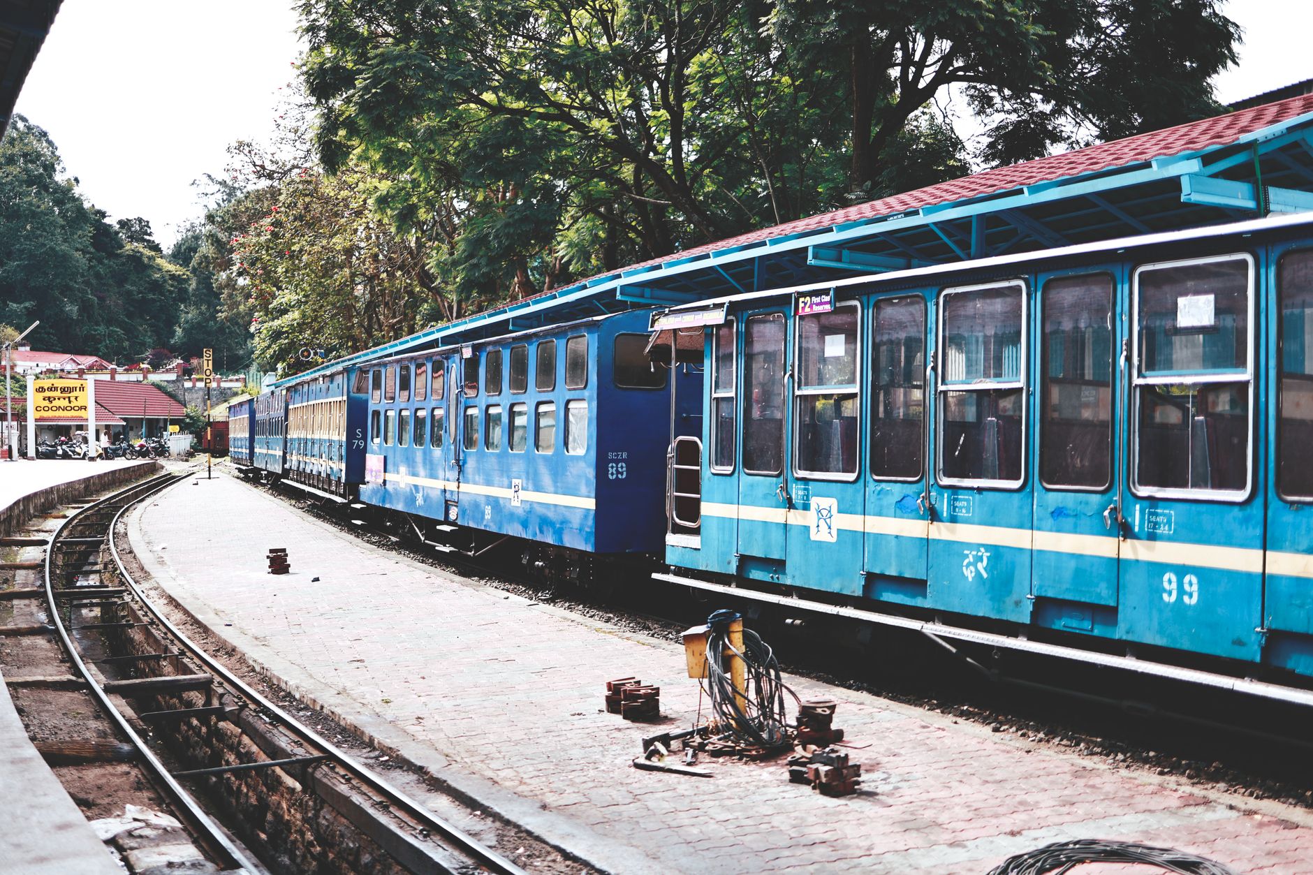 Scenic view of a blue train at Ooty Railway Station amidst lush greenery.