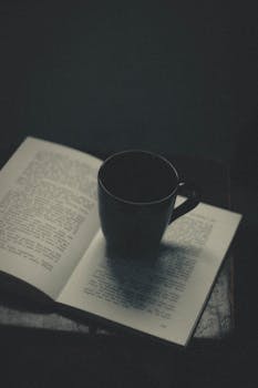 一本打开的书上放着一个陶瓷马克杯，这场景温暖而迷人，非常适合安静的阅读时光