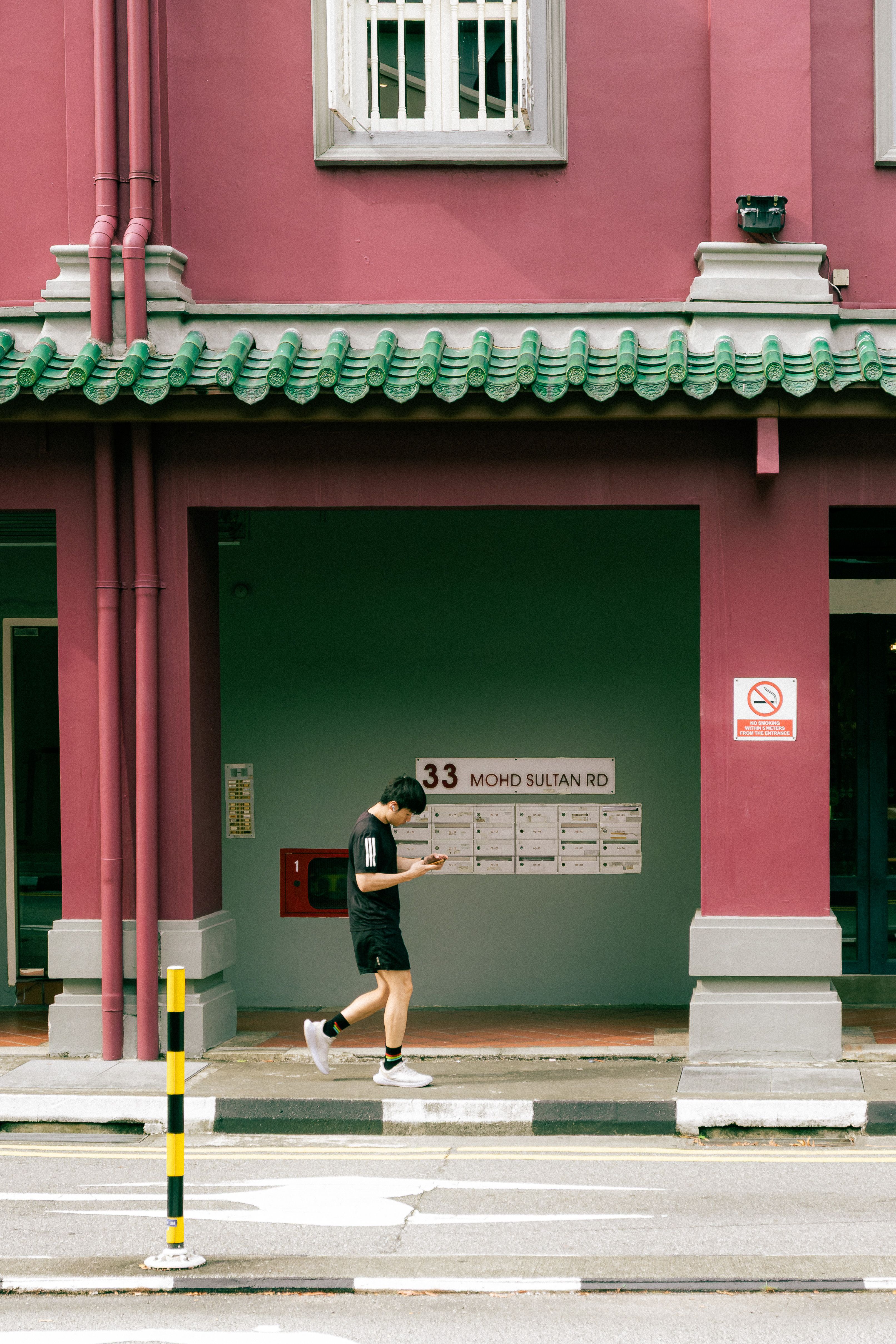 A person walking by the vibrant architecture of Mohd Sultan Rd in Singapore, using a smartphone.