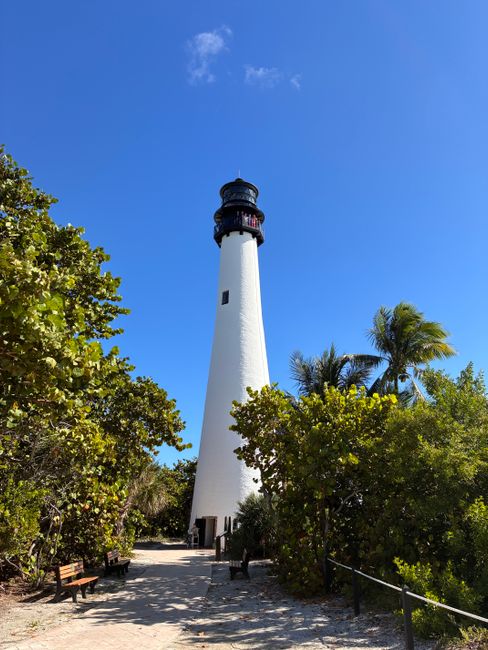 Scenic view of Cape Florida Lighthouse in Key Biscayne surrounded by greenery under a clear blue sky.