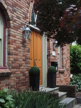 A classic brick house entrance with vibrant orange door and greenery in Doylestown.