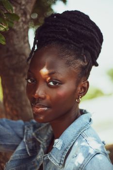 A beautiful portrait of a woman with natural hair wearing a denim jacket, taken outdoors.