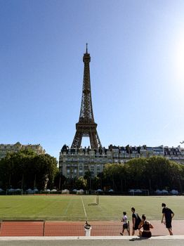 Scenic view of the Eiffel Tower with people relaxing in a Parisian park on a sunny day.