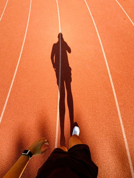 A runner's long shadow across a track at sunset — photo by Prateek Katyal on Pexels