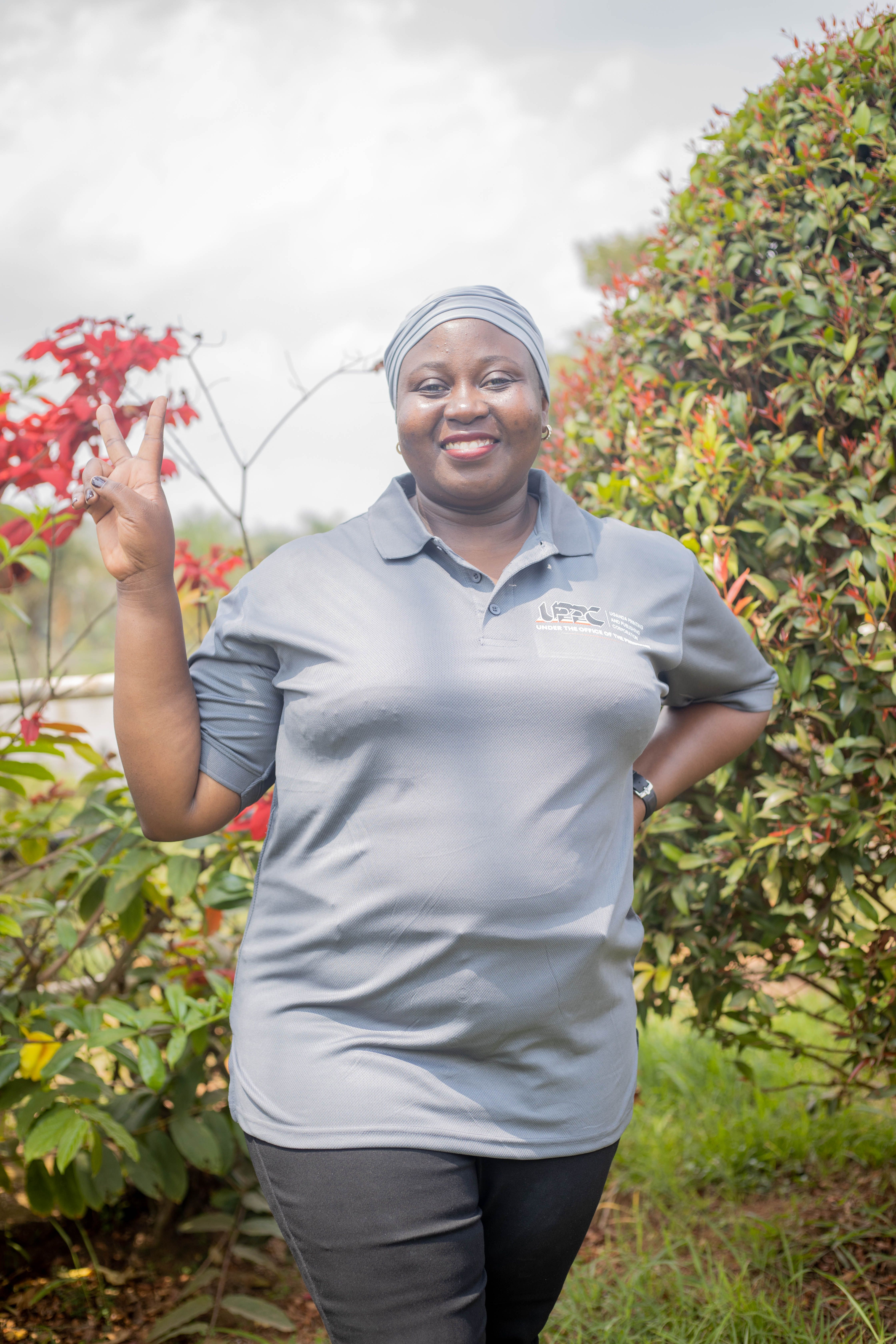 A woman standing in a garden smiles while flashing a peace sign. Bright and cheerful.