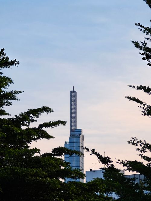 Free A towering skyscraper surrounded by tree foliage at sunrise, showcasing urban nature fusion. Stock Photo