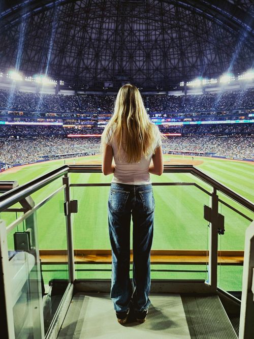 Free A woman stands at a stadium balcony, watching a baseball game under bright lights. Stock Photo