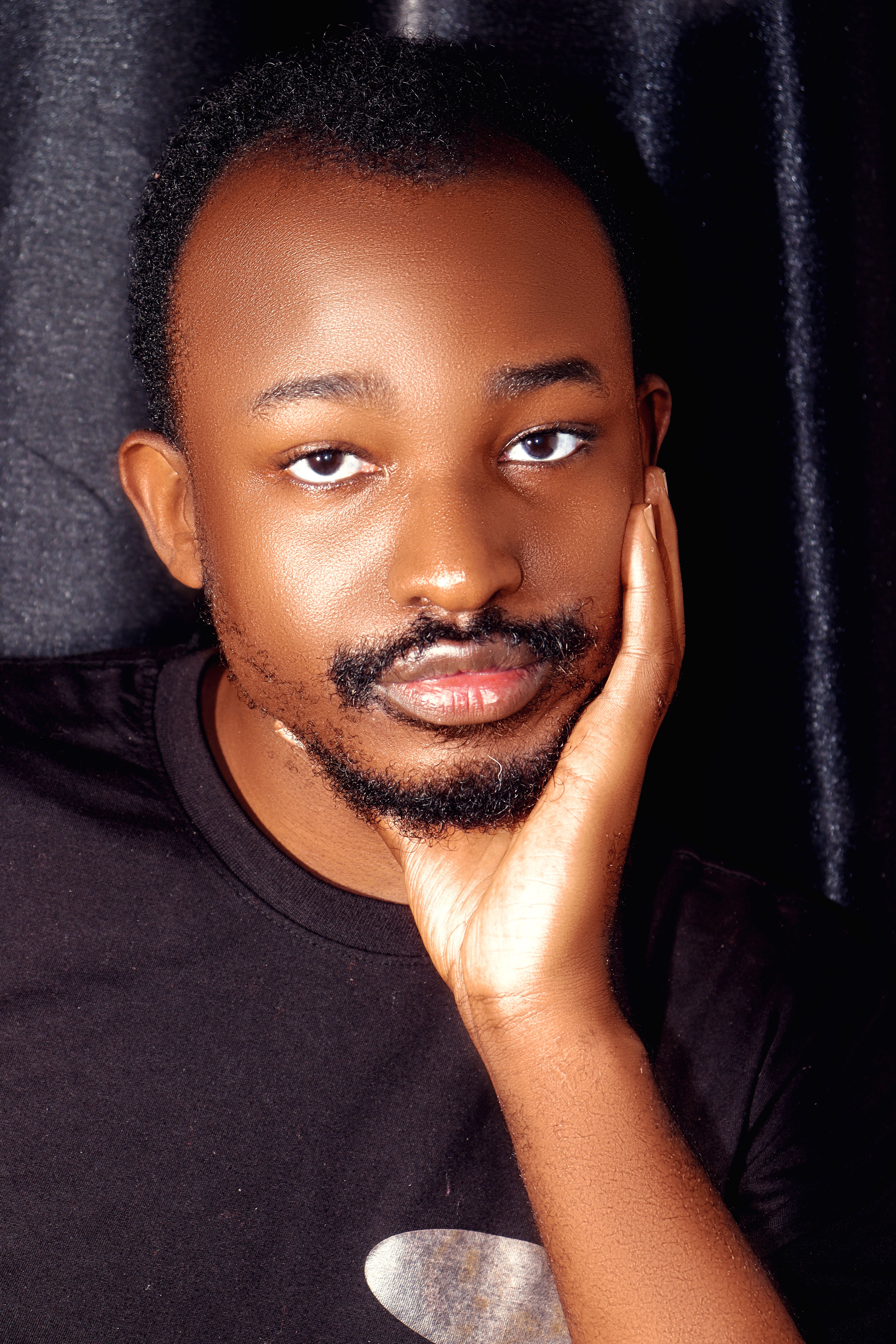 Close-up portrait of a young man resting his face on his hand against a dark background.