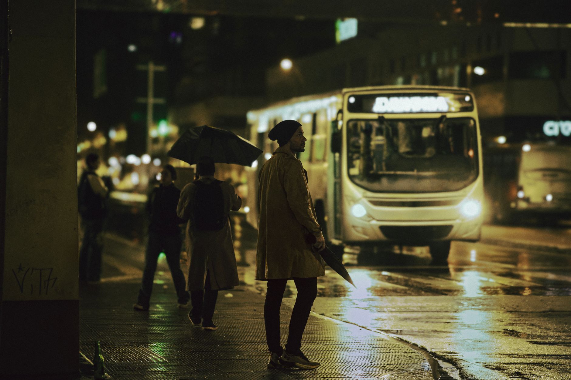 A vibrant night scene in Maringá, Brazil, with people and a bus on a rainy street.