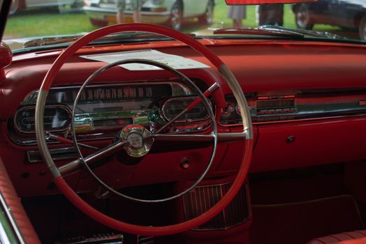 Close-up view of a vintage car's red interior dashboard with a classic steering wheel.