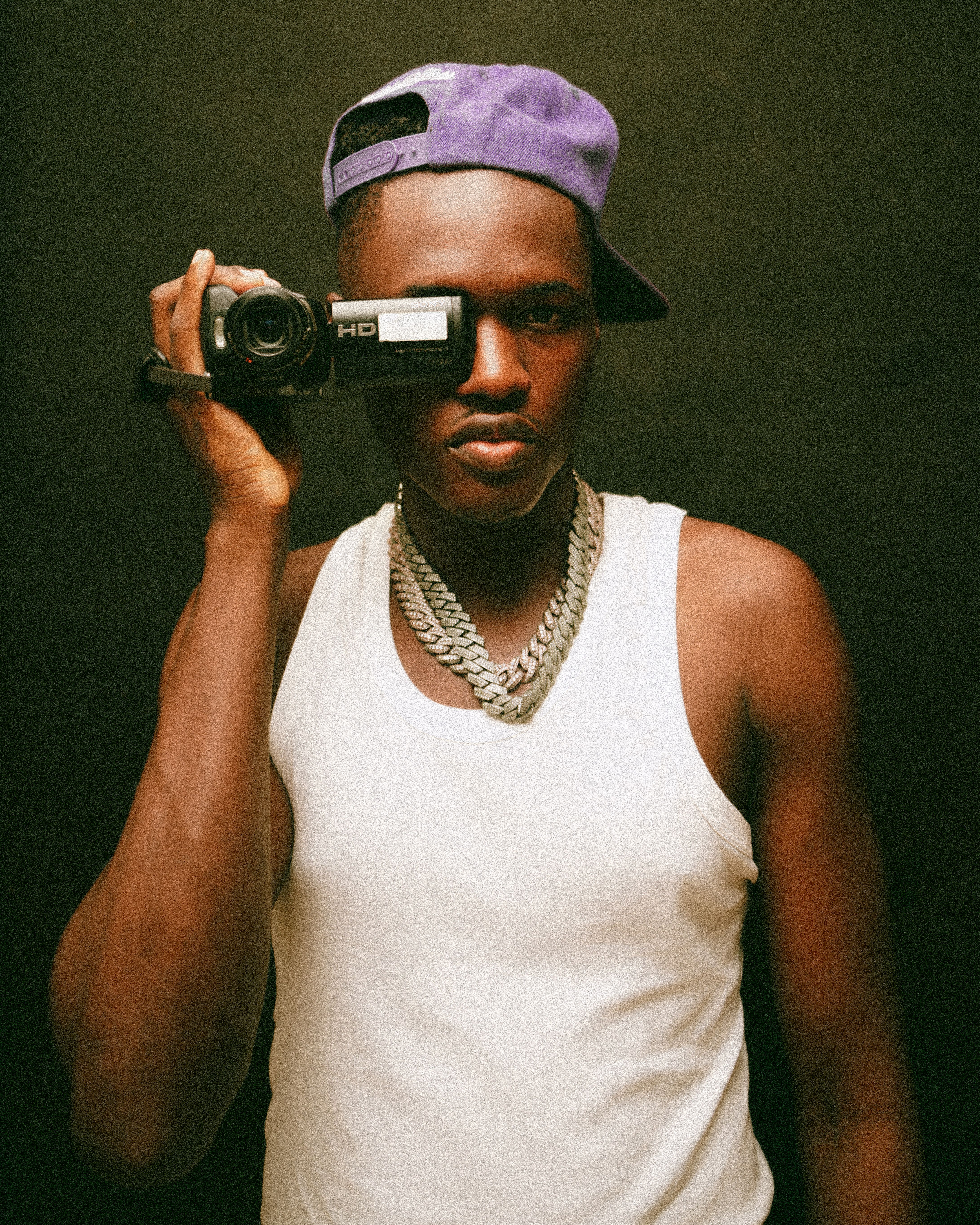 Portrait of a young man using a video camera, wearing a tank top and cap.
