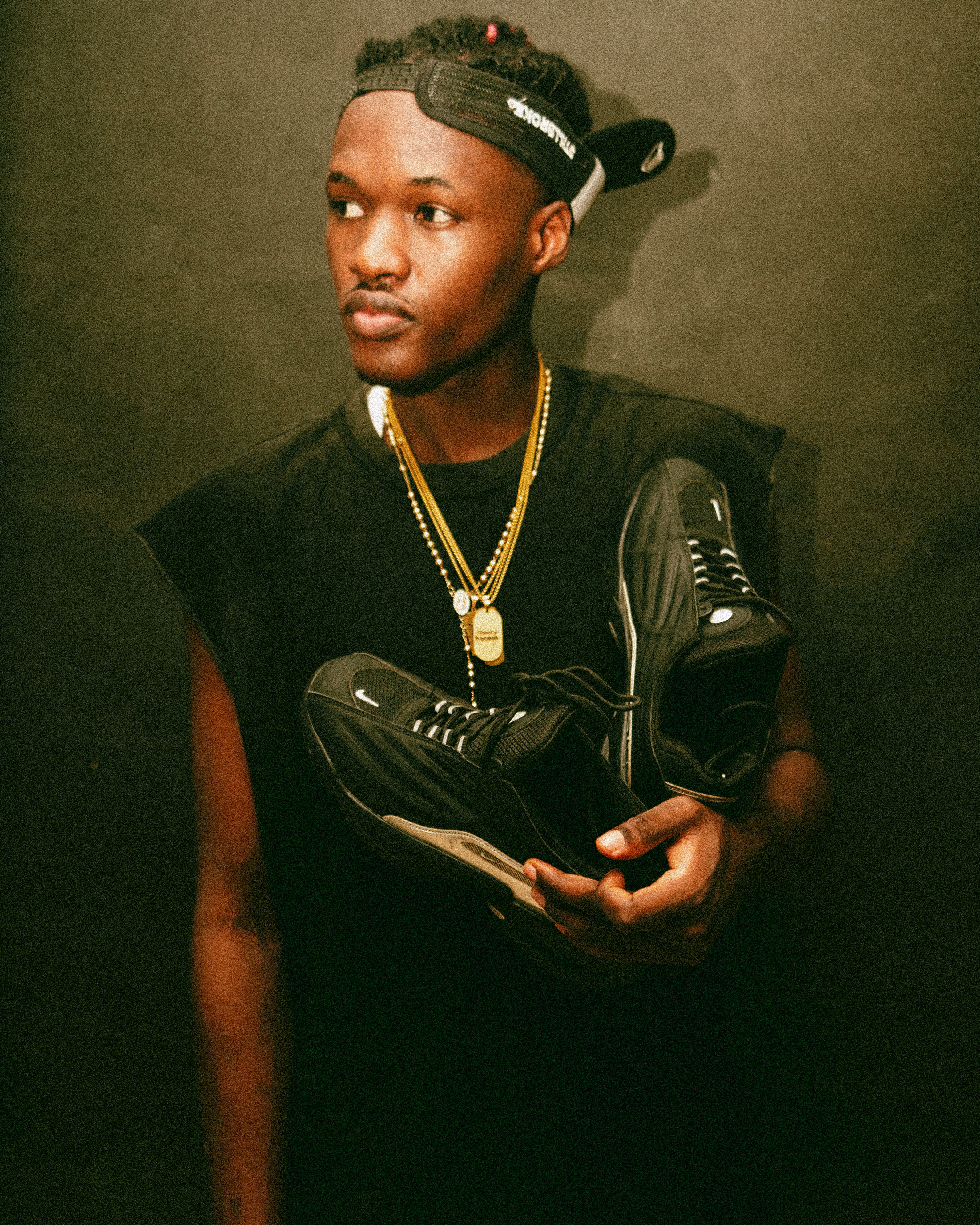 Young man in casual attire holding black sneakers, exuding fashion and urban style.