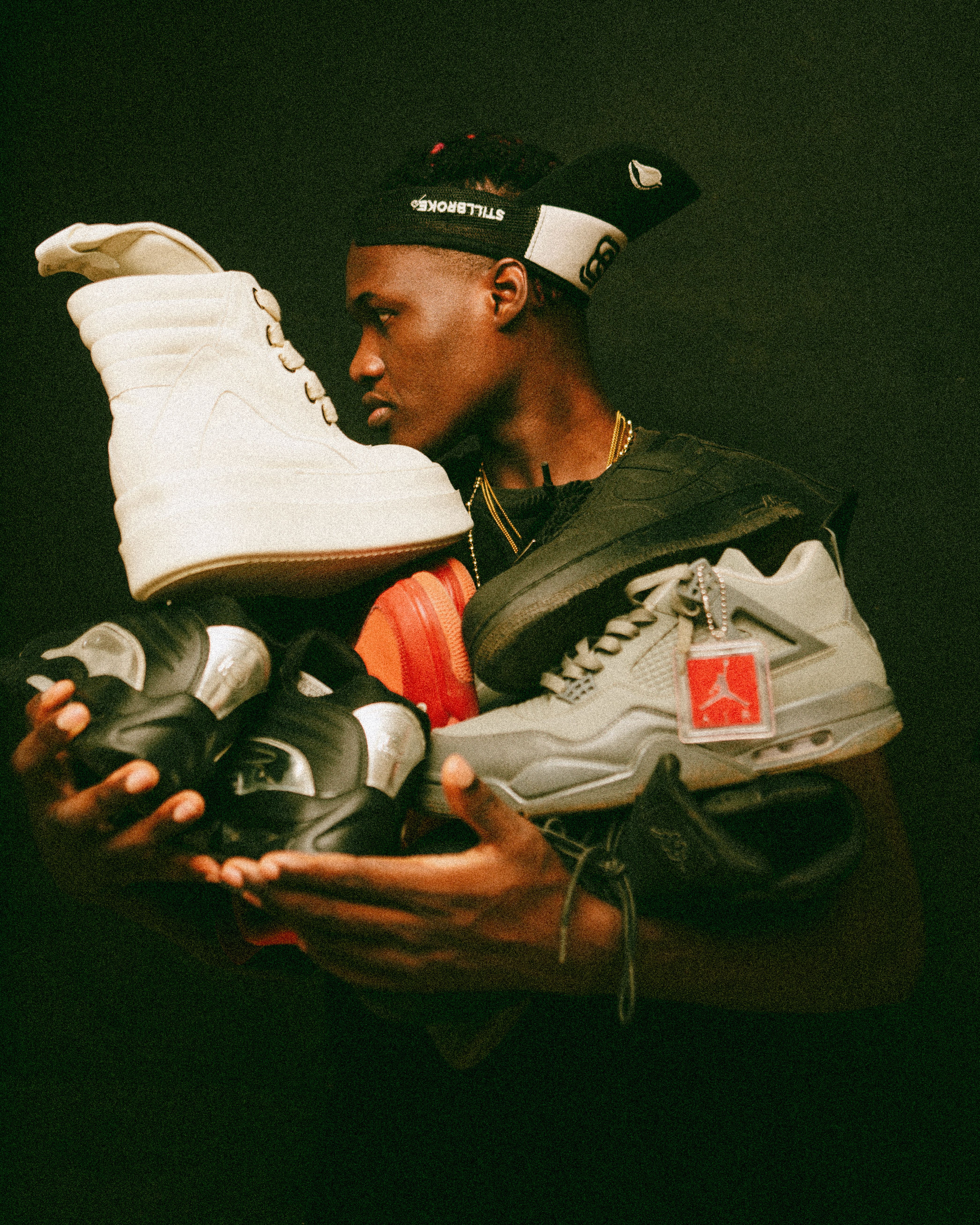 A stylish young man showcasing a diverse collection of trendy sneakers against a dark background.