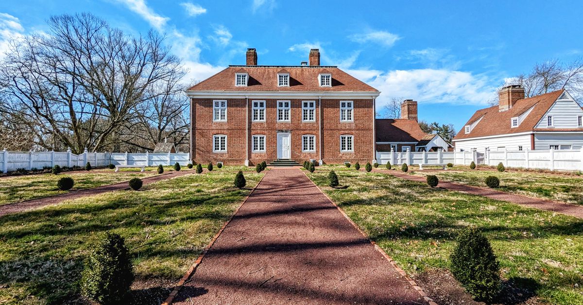Explore a well-preserved colonial mansion surrounded by a scenic garden under a clear sky.