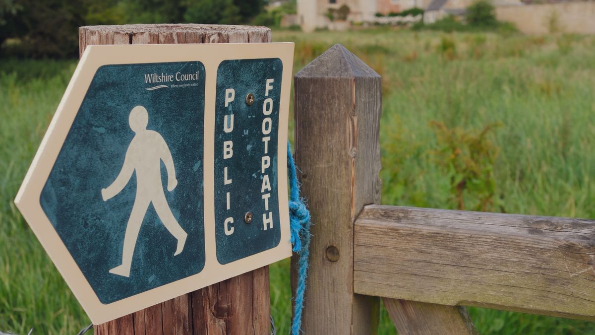 A public footpath sign beside a field gate in the English countryside, the start of a walking weekend in the Cotswolds