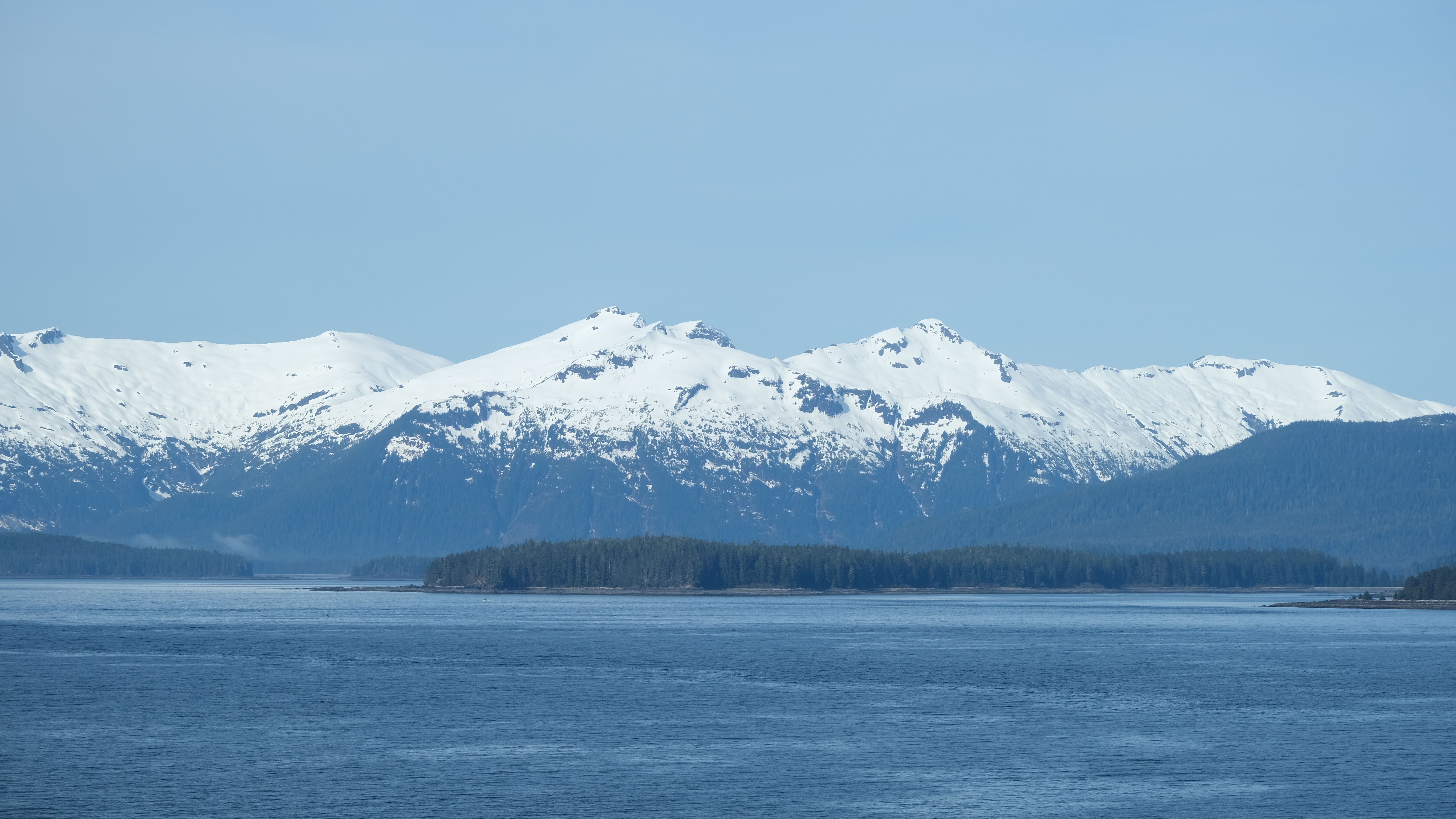 Spectacular view of snow-capped mountains in Alaska with a serene water foreground under clear blue skies.