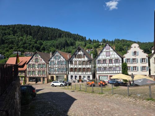 Free Charming half-timbered houses in Schiltach, Germany under a clear blue sky, with scenic forest backdrop. Stock Photo