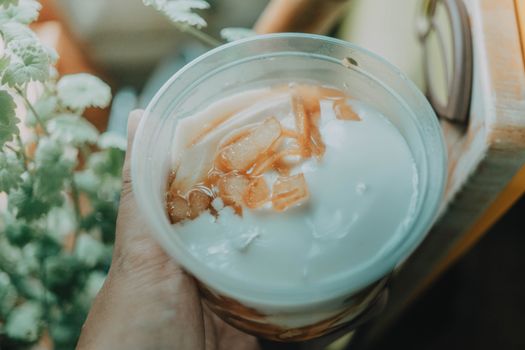 Close-up of a hand holding a cup containing a creamy coconut dessert with sliced toppings.