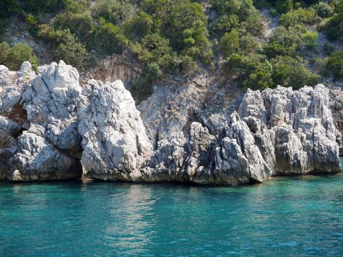 Free Rocky coastal cliffs by the sea with clear turquoise water and lush greenery. Stock Photo