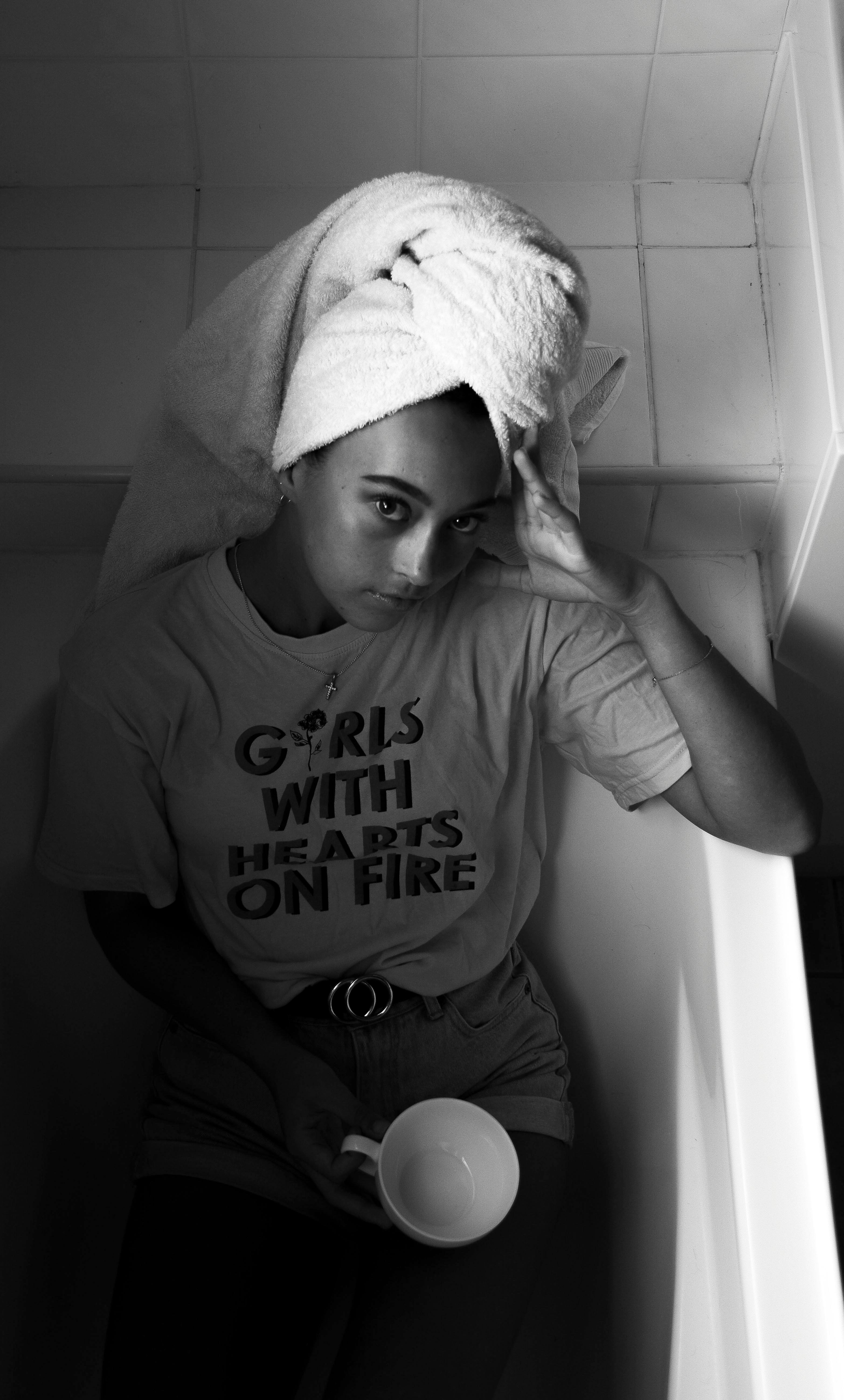 一个女人头上包着毛巾，坐在浴缸里，手里拿着一个马克杯，画面是单色的