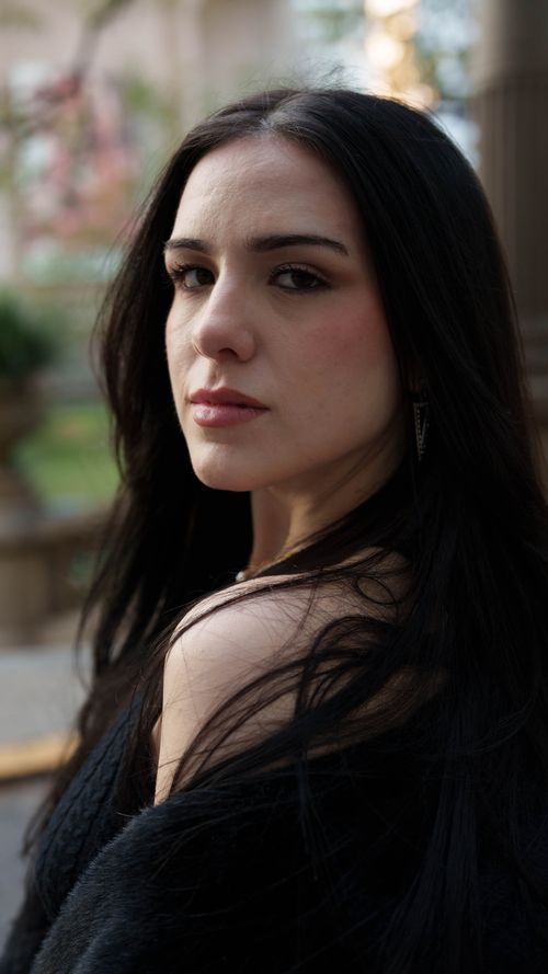 Free Elegant portrait of a woman with long black hair and an intense gaze, outdoors in soft lighting. Stock Photo