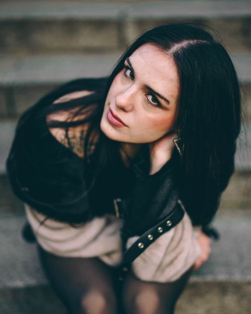 Free Stylish woman sitting on stone steps outdoors, looking up at the camera. Stock Photo