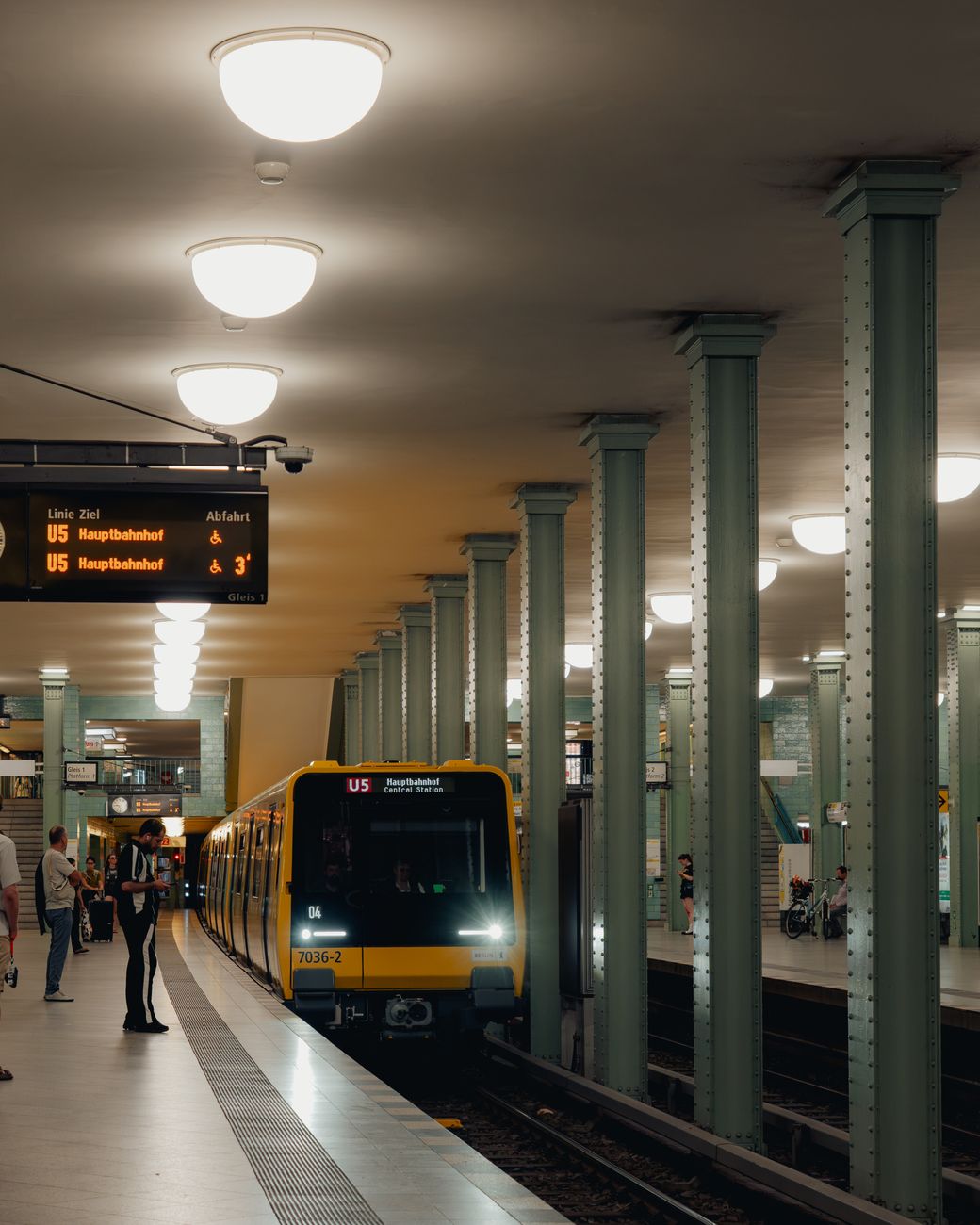 U-Bahn halte in Berlijn toont een aankomende gele trein in de nacht met wachtende passagiers.