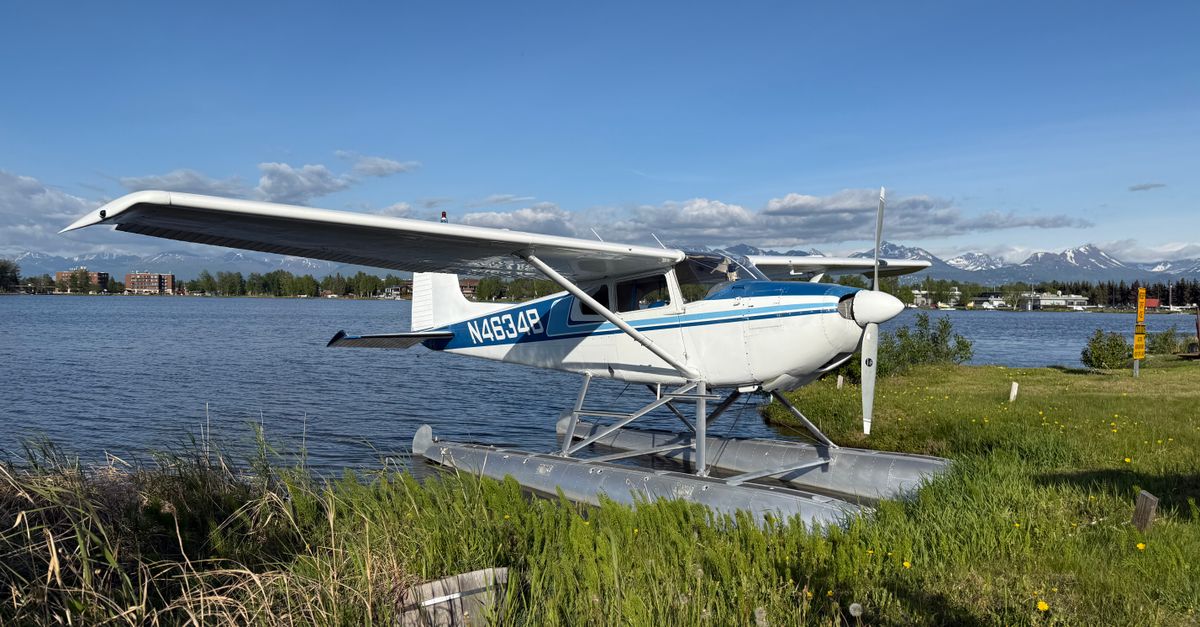 A scenic view of a seaplane docked by a lake, framed by distant mountains under a blue sky.