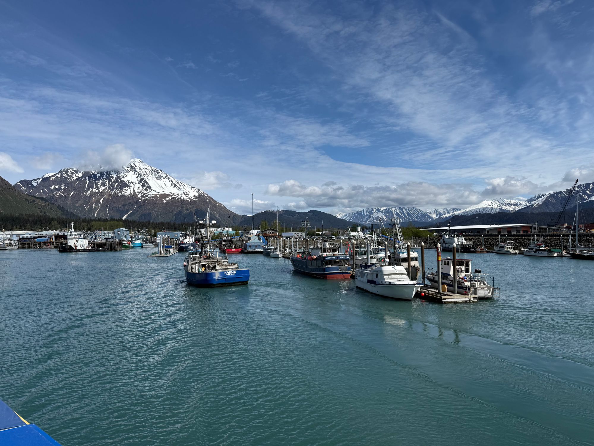Boats docked at Seward harbor with scenic mountains and a clear blue sky in the background.